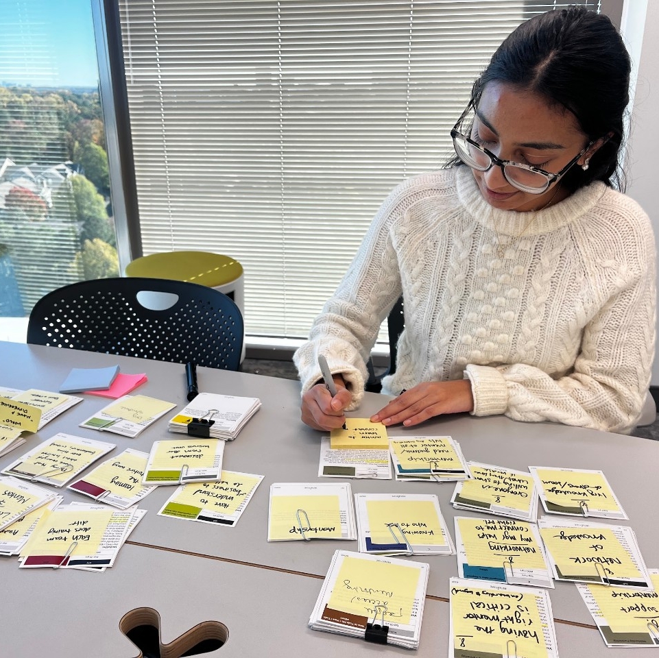 a student sits at a desk with a bright window behind, sorting cards into piles while writing post it note labels.